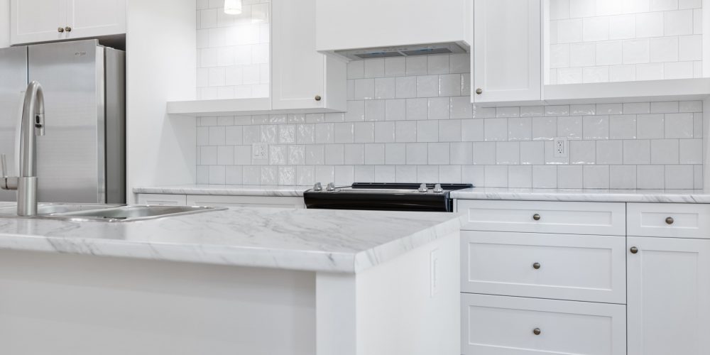 Close up of a white kitchen island in front of a a white counter with white cabinetry above