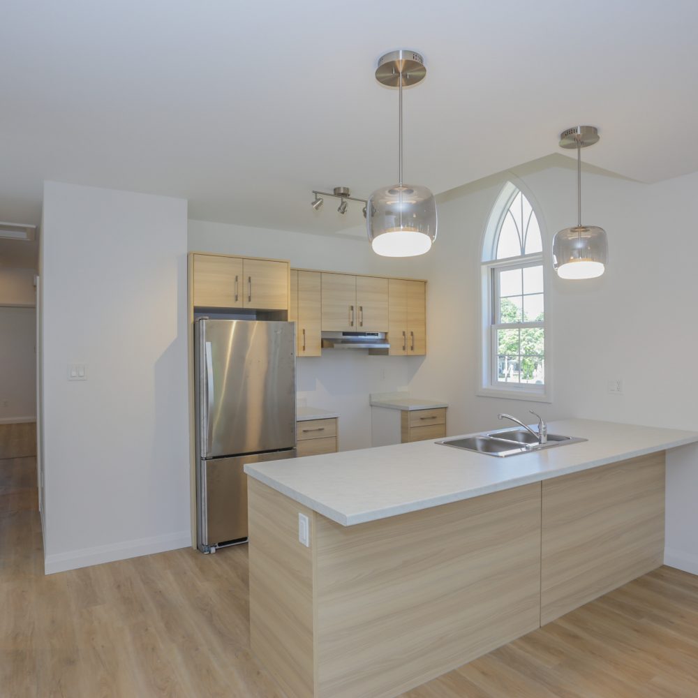 Interior of a custom kitchen with light wood cabinetry, marble countertop and stainless steel fridge beside a two-door closet