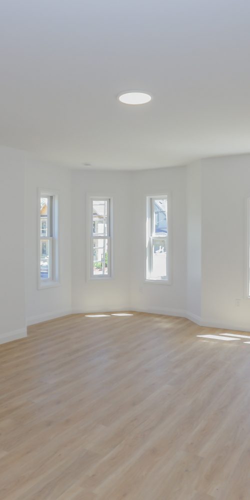 Interior of a large room with white walls, hardwood floors and bow windows